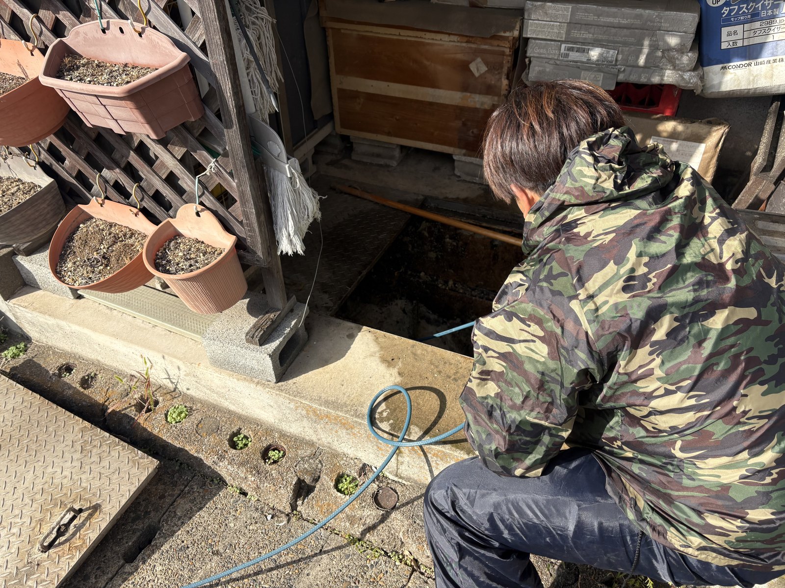 マンションの屋外に設けられた排水枡を開けて内部を確認している様子